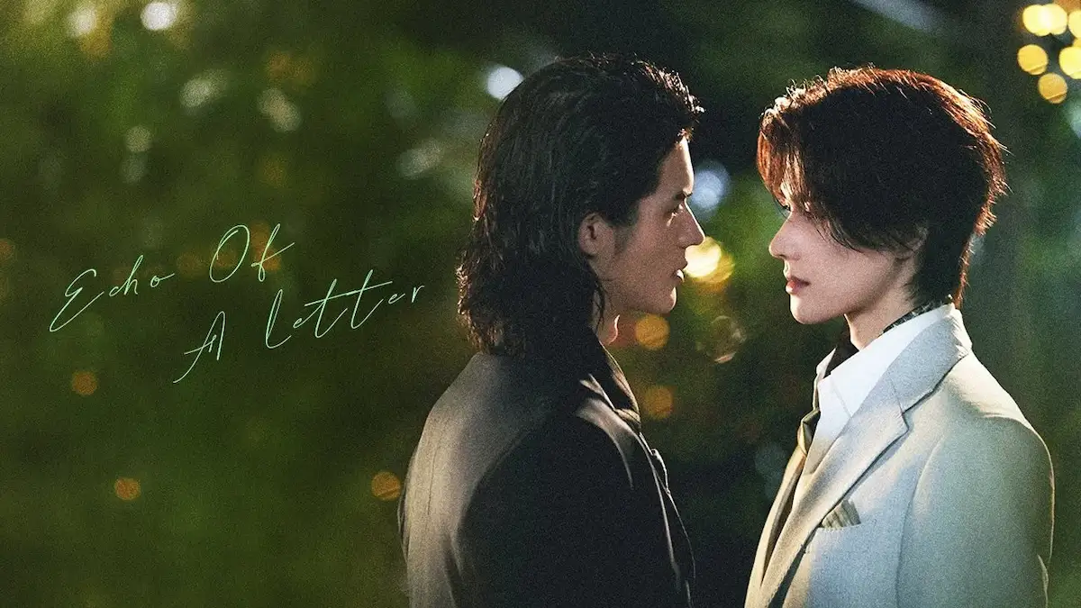Close-up portrait of two male leads in an Asian BL romance drama, one in a dark jacket and the other in a light grey blazer, looking closely at each other outdoors