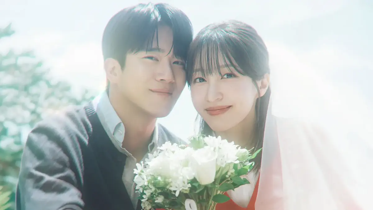 A smiling young man and woman leaning heads together holding a bouquet of white flowers in bright sunlight