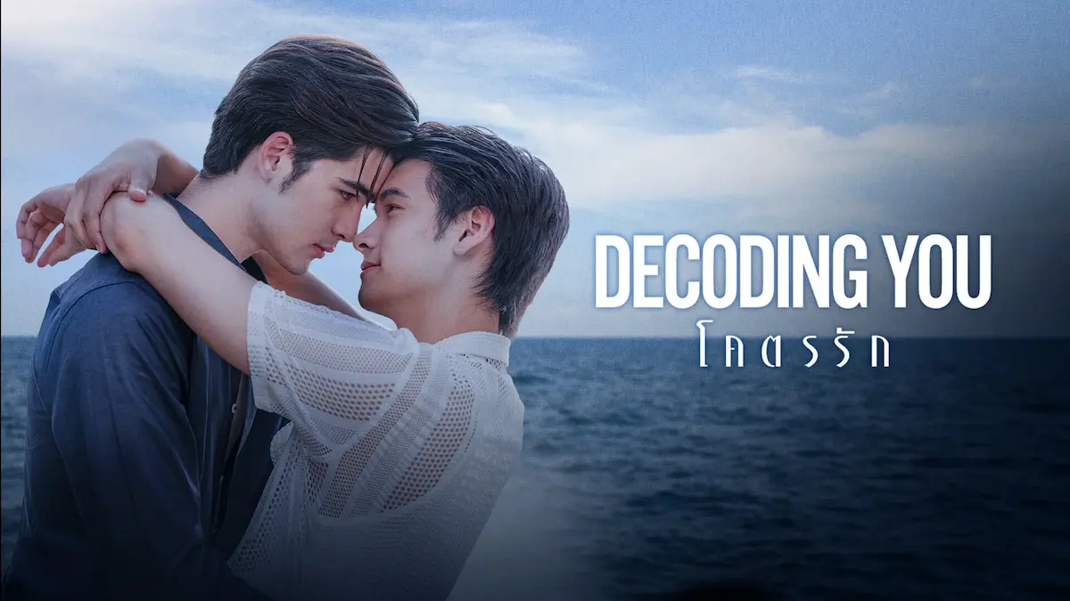 Two men holding each other closely by the ocean against a blue sky beside white title text reading Decoding You and Thai script