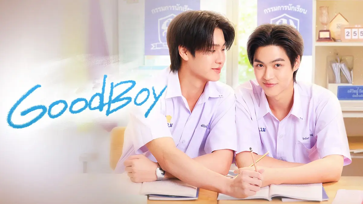 Two male students in white uniforms sitting together at a classroom desk with blue handwritten text reading Good Boy